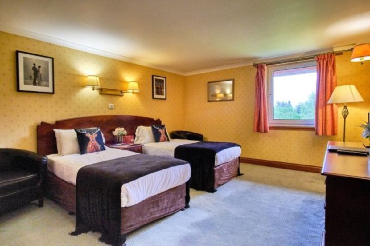 A hotel room with two beds, a desk, a chair, and a window with curtains.