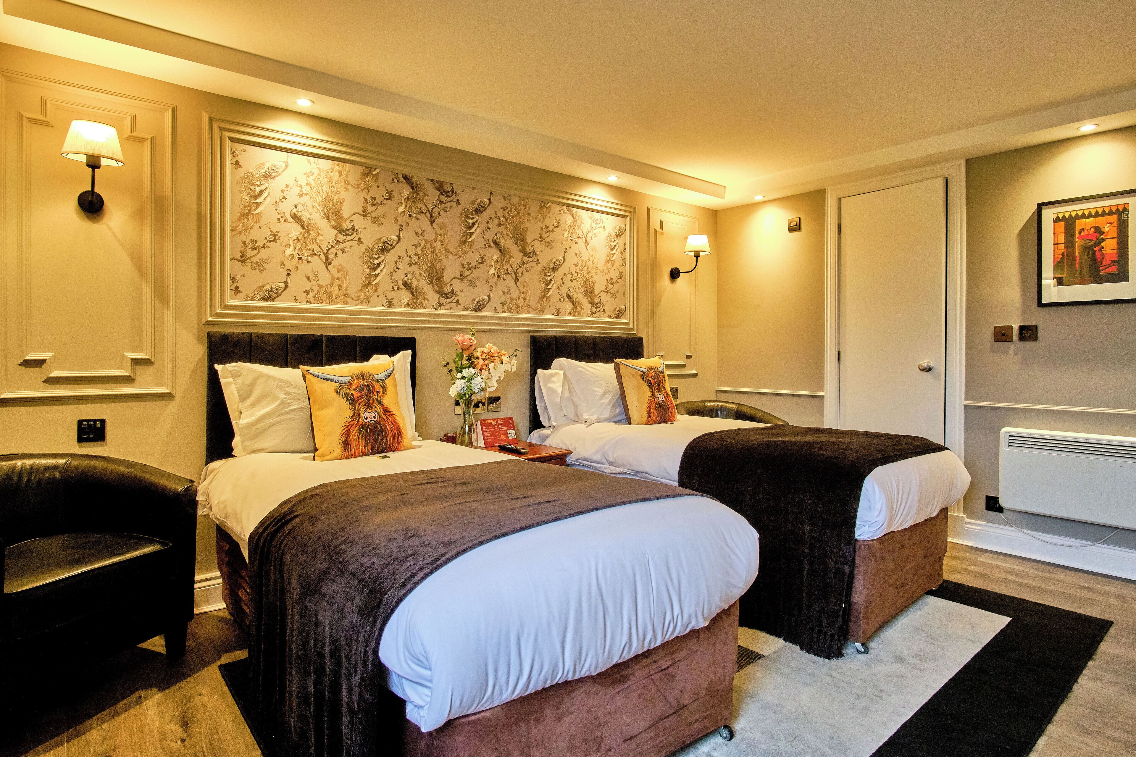 Ein Hotelzimmer mit zwei Betten, floralem Wandpapier und einem schwarzen Ledersessel.