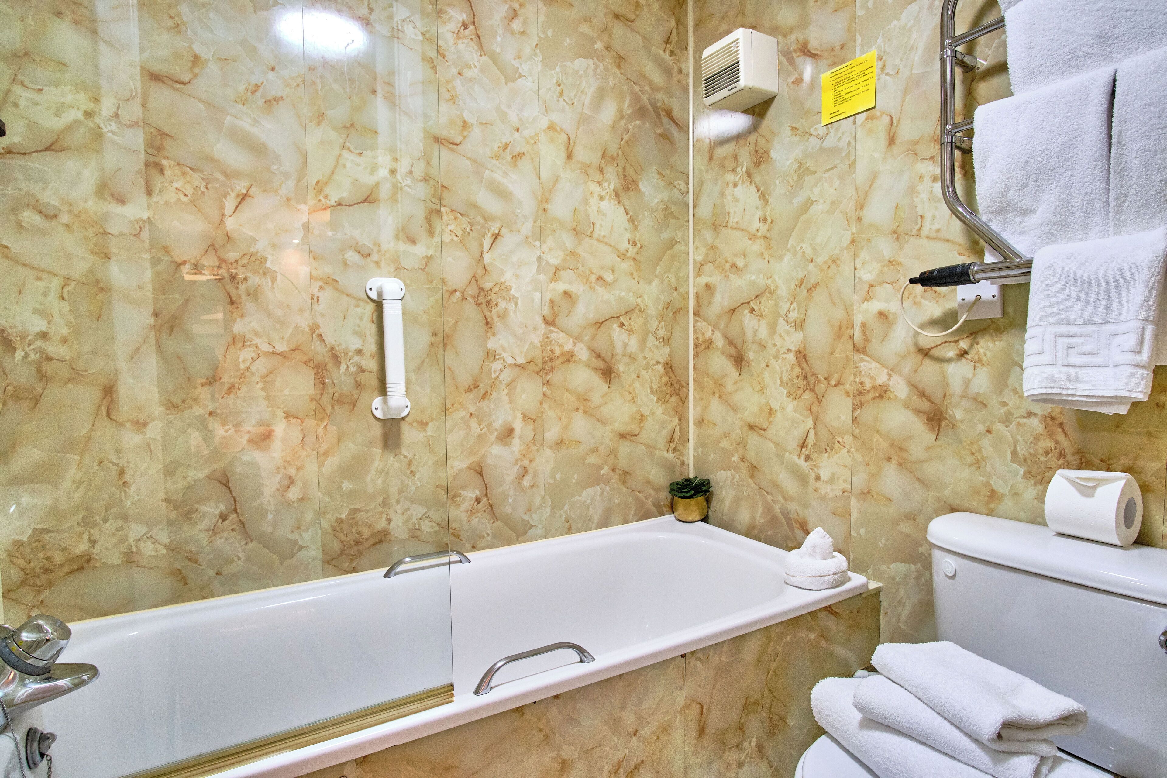 Un baño con pared de mármol, una bañera, un inodoro y un perchero para toallas.