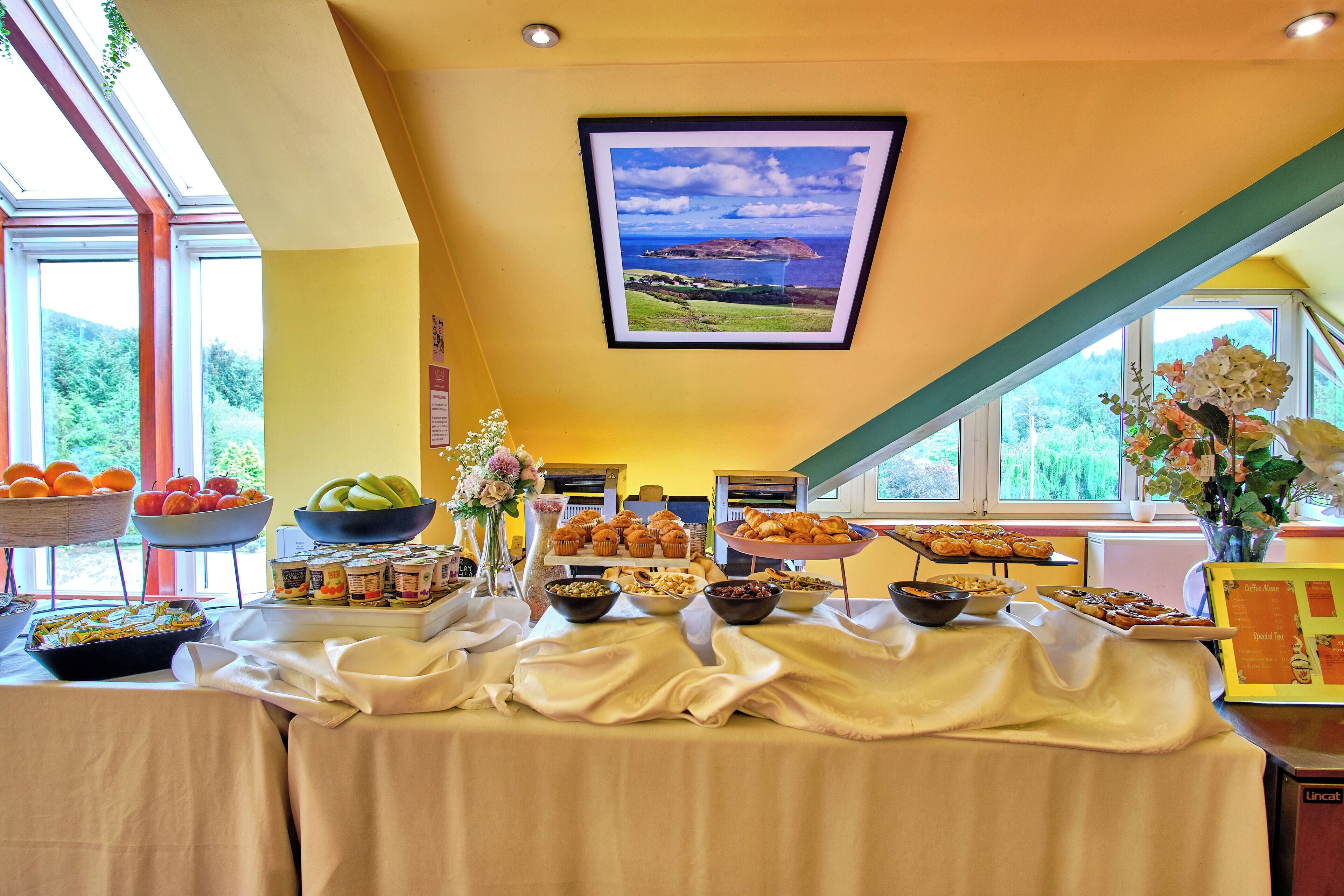 A buffet table with various food items and a framed landscape picture on the wall.