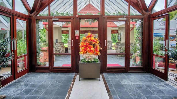 Una entrada de hotel con fachada de vidrio, un centro de flores y un camino de piedra que lleva a las puertas.