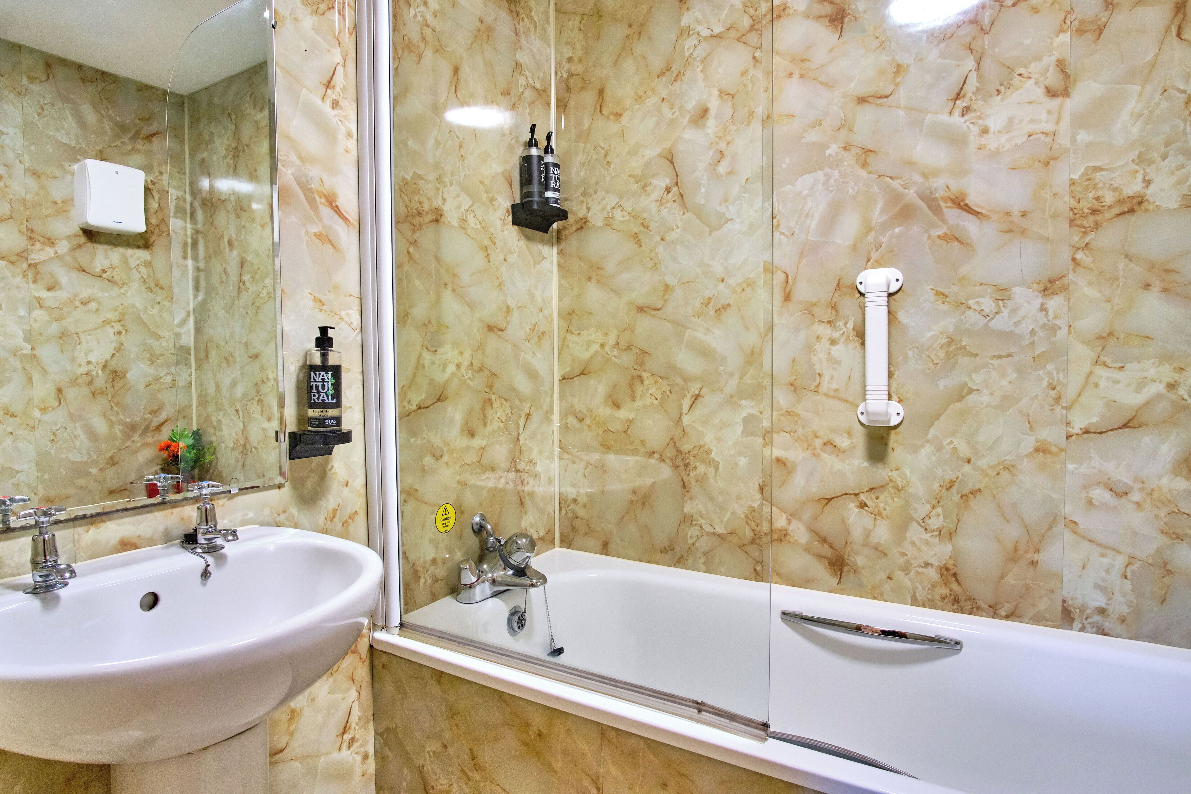 Une salle de bain avec un mur en marbre, un lavabo, un miroir et une baignoire.