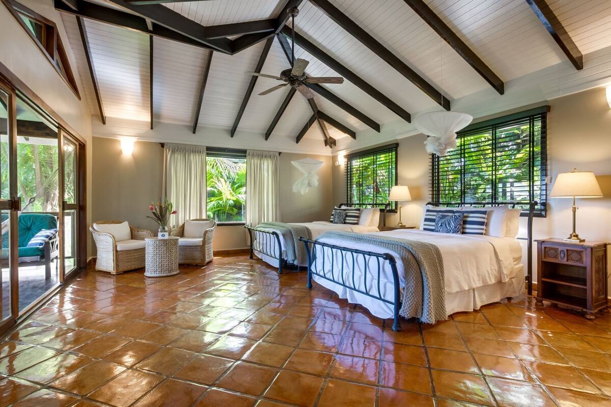 Quarto espaçoso com uma cama grande, um ventilador de teto e vista para um verde exuberante pelas janelas.