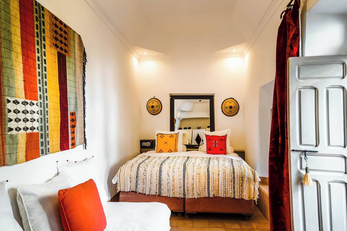 A bedroom with a bed, pillows, a bedside table, a wall hanging, and a door.