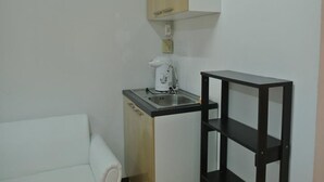 Eine kleine Küchenzeile mit Spüle, Kaffeemaschine und einem Holzschrank über der Arbeitsfläche.