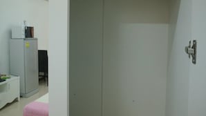 Ein Zimmer mit geschlossener Tür, einem kleinen Schreibtisch mit einem Computer und einem Kühlschrank.