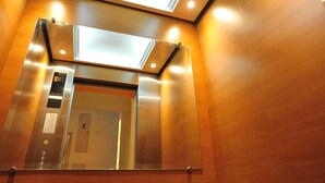 An elevator interior with a reflective metallic finish, a control panel, and a door with a number. - The Garden Living (Bangkok)