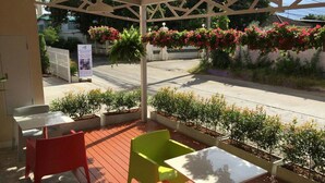 An outdoor seating area with a covered patio, a white fence, and hanging flower baskets. - The Garden Living (Bangkok)