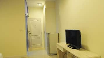 A hallway with a door, a small refrigerator, and a TV on a wooden stand.
