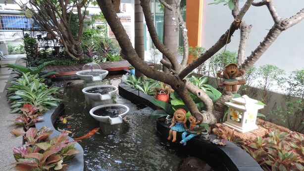 A tranquil indoor garden with a small pond, decorative trees, and a swing set. - The Garden Living (Bangkok)