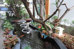 A tranquil indoor garden with a small pond, decorative trees, and a swing set. - The Garden Living (Bangkok)