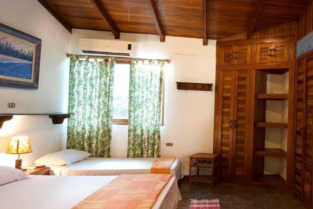 Une chambre avec deux lits, une armoire en bois, une petite table et une fenêtre avec des rideaux.