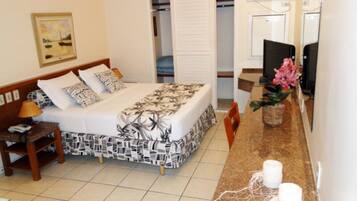 A hotel room with a bed, bedside table, lamp, and a small desk with a chair.