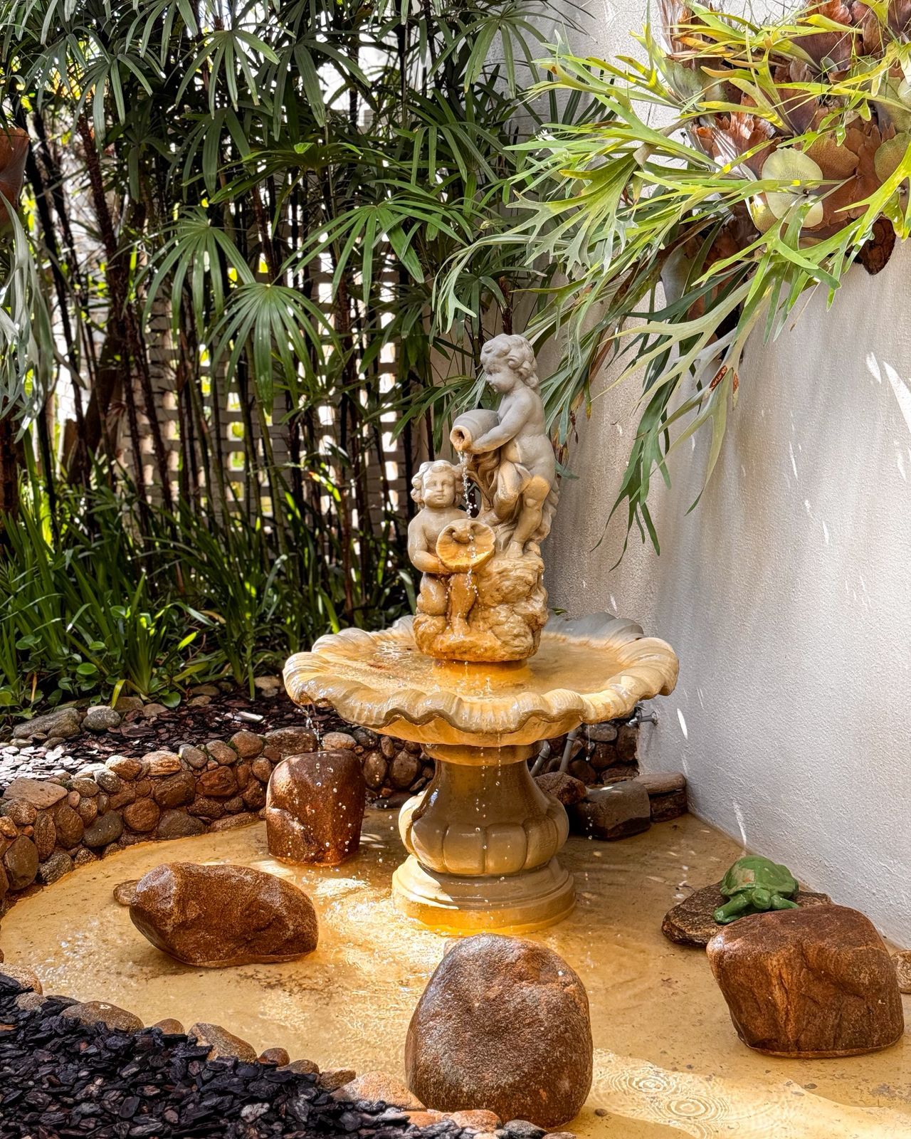 A stone fountain with a sculpture of cherubs, surrounded by rocks and foliage.