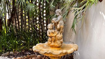 Una fuente de piedra con una escultura de querubines, rodeada de rocas y follaje.