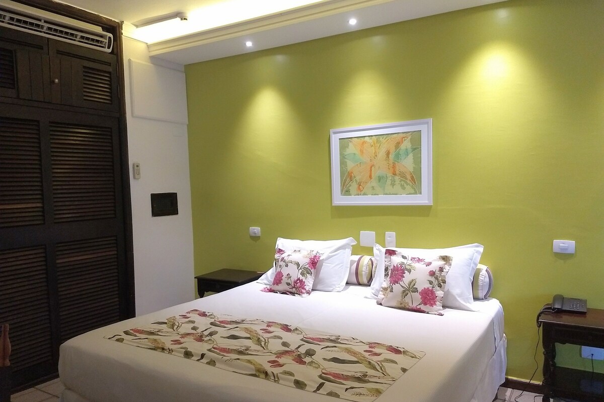 A hotel room with a bed, a nightstand, a phone, and a painting on the wall.