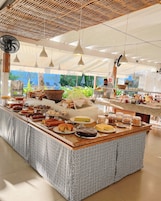 Un bufé con diversas opciones de comida, un mantel estampado, luces colgantes y vistas al exterior.