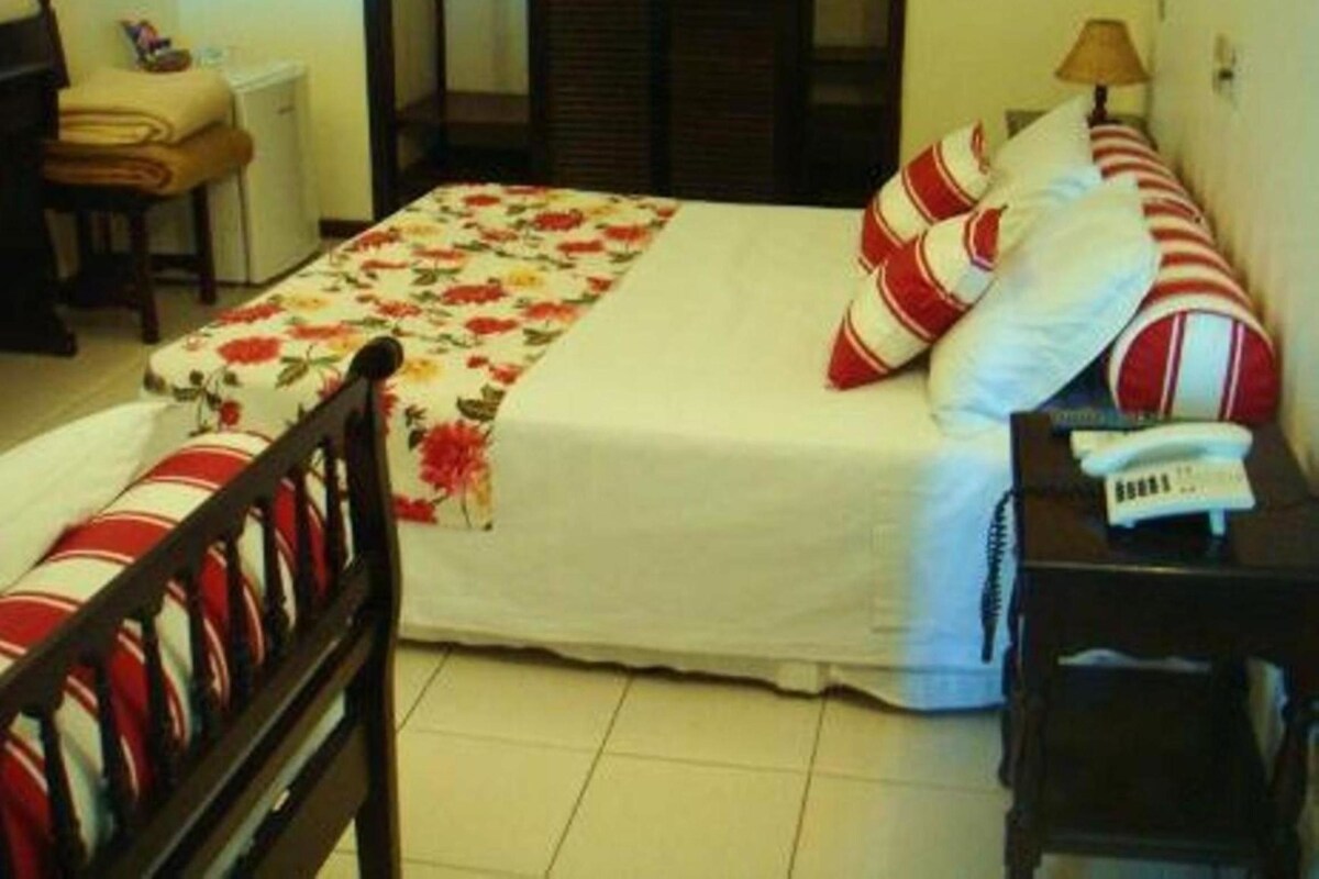A hotel room with a bed, a chair, a bedside table with a lamp, and a telephone.