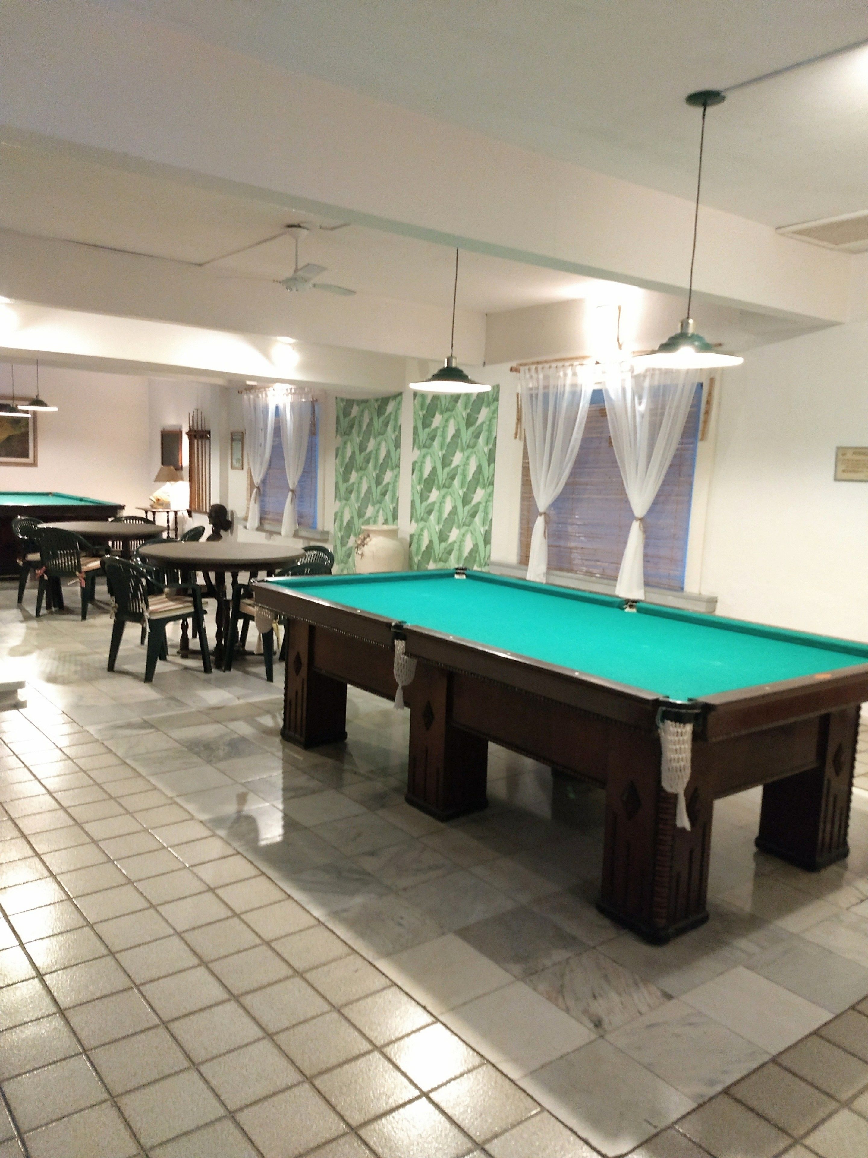 A pool table area with multiple tables and chairs, a ceiling fan, and a tiled floor.