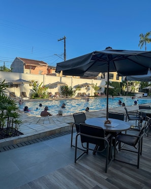 A pool area with lounge chairs and umbrellas, surrounded by buildings. - Ubatuba Palace Hotel (Ubatuba)