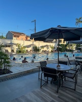 Zona de piscina con sillas de descanso y sombrillas, rodeada de edificios.