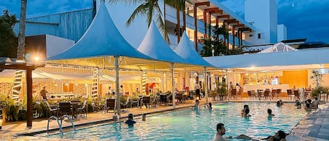 A hotel pool area with a large pool, lounge chairs, and a covered seating area.