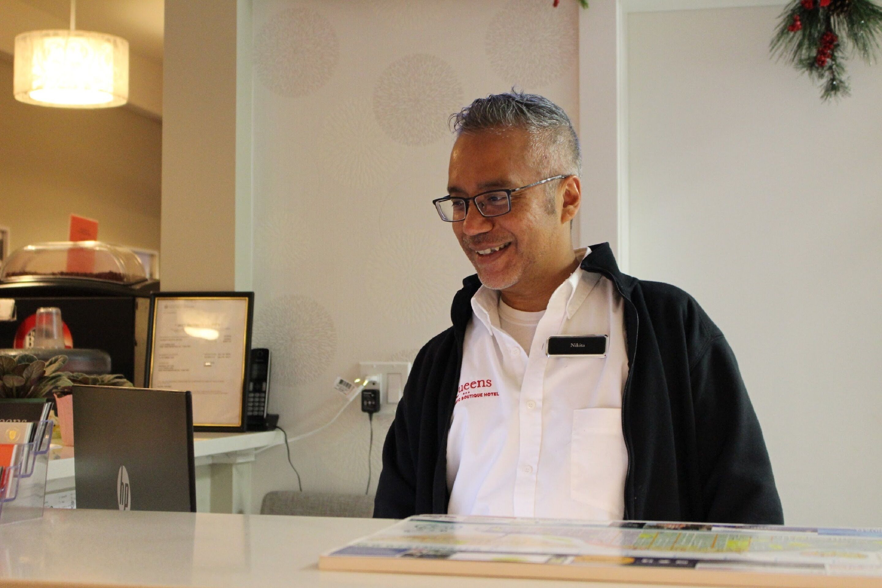 Een receptiebalie van een hotel met een laptop, een ingelijst certificaat en een naambadje op de toonbank.