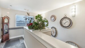 Un espace d’accueil d’hôtel au design moderne, comprenant un comptoir de réception, plusieurs horloges murales, une grande fenêtre offrant une vue dégagée et une plante en pot.