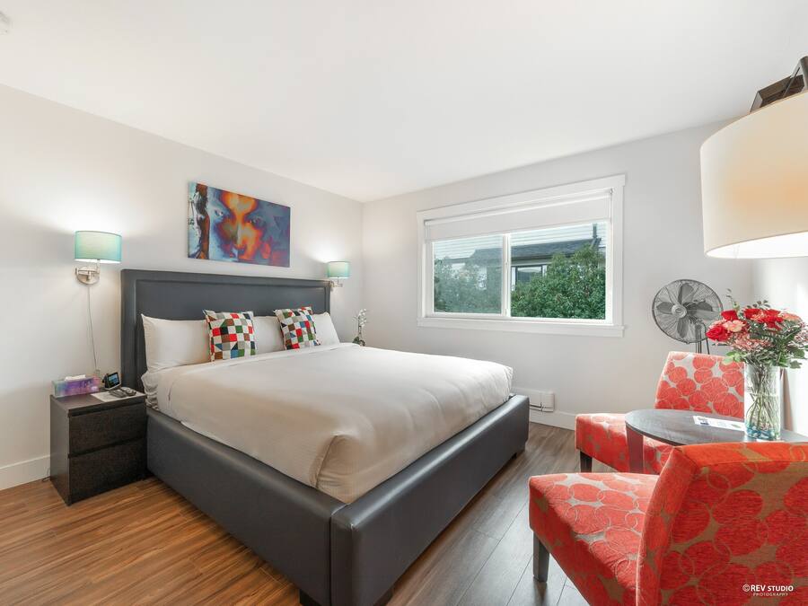 A modern bedroom with a large bed, bedside tables, a chair, a table, and a window with a view of greenery.