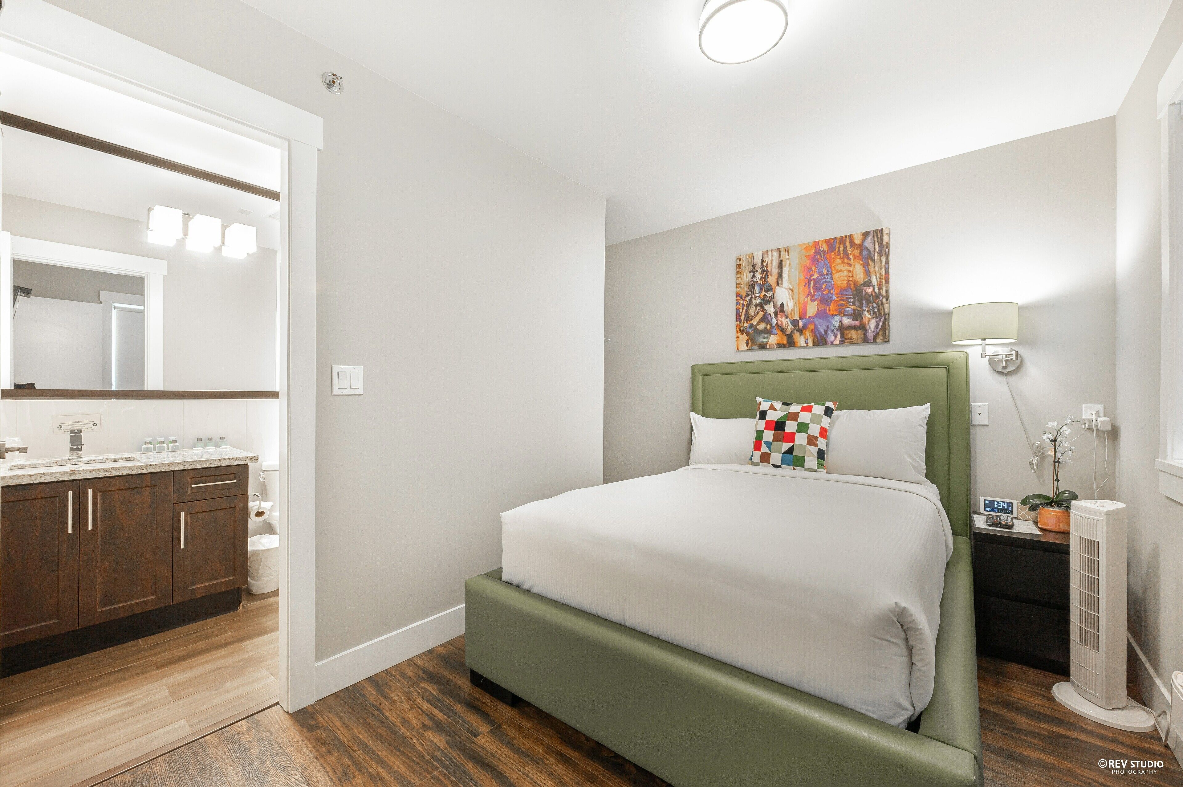 Una habitación de hotel moderna con una cama grande, un baño con tocador y un cuadro en la pared.