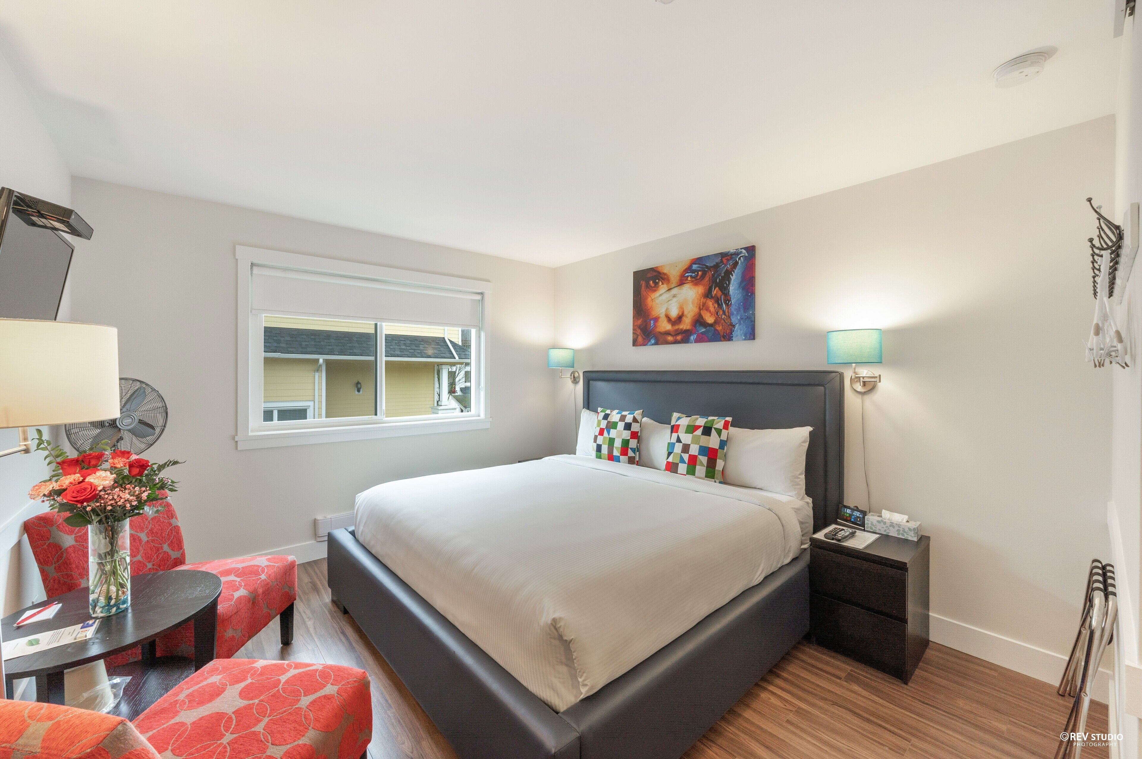 A modern hotel room with a large bed, bedside tables, a desk with a chair, and a window.