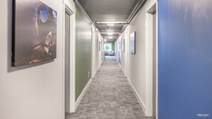 A long, narrow hallway with a patterned carpet, white walls, and a blue accent wall. - Queens Hotel (New Westminster)