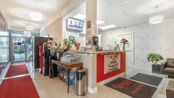 A hotel reception area with a red and white color scheme, a reception desk, a TV screen, and a coffee machine.