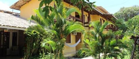 A yellow building with a tiled roof, surrounded by lush greenery and a stone pathway.