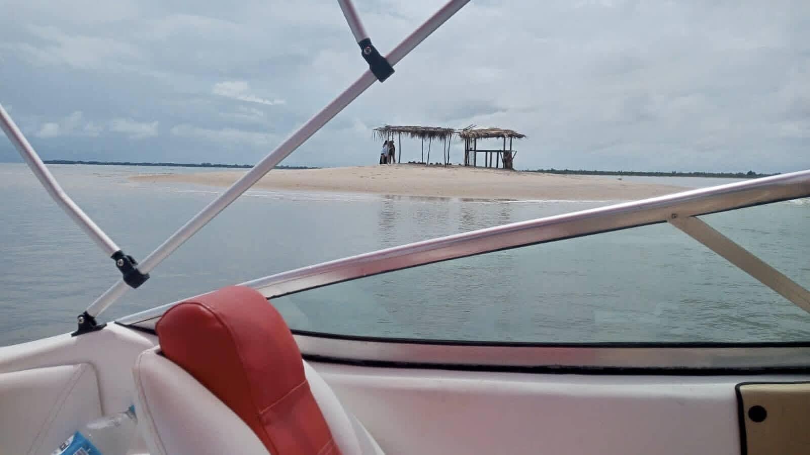 El interior de un barco con vista a una playa y una estructura de techo de paja en la distancia.