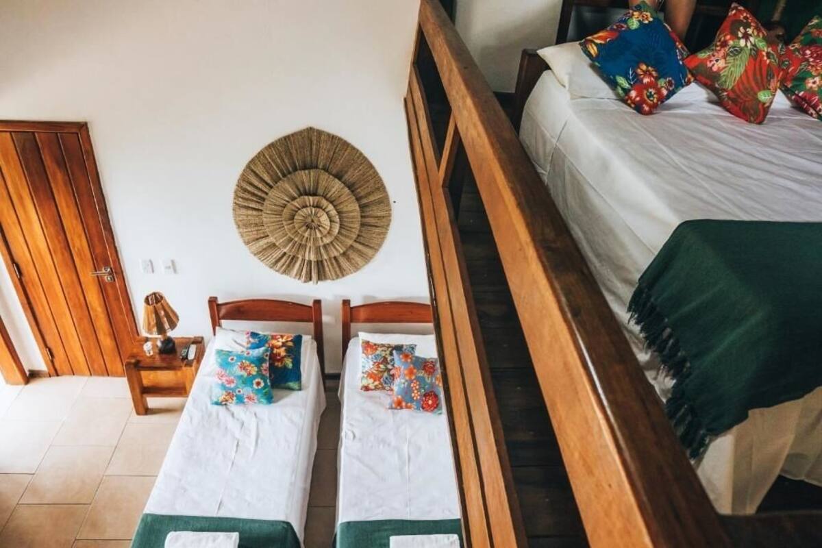 A room with two single beds, a wooden headboard, a woven wall hanging, and a nightstand with a lamp.