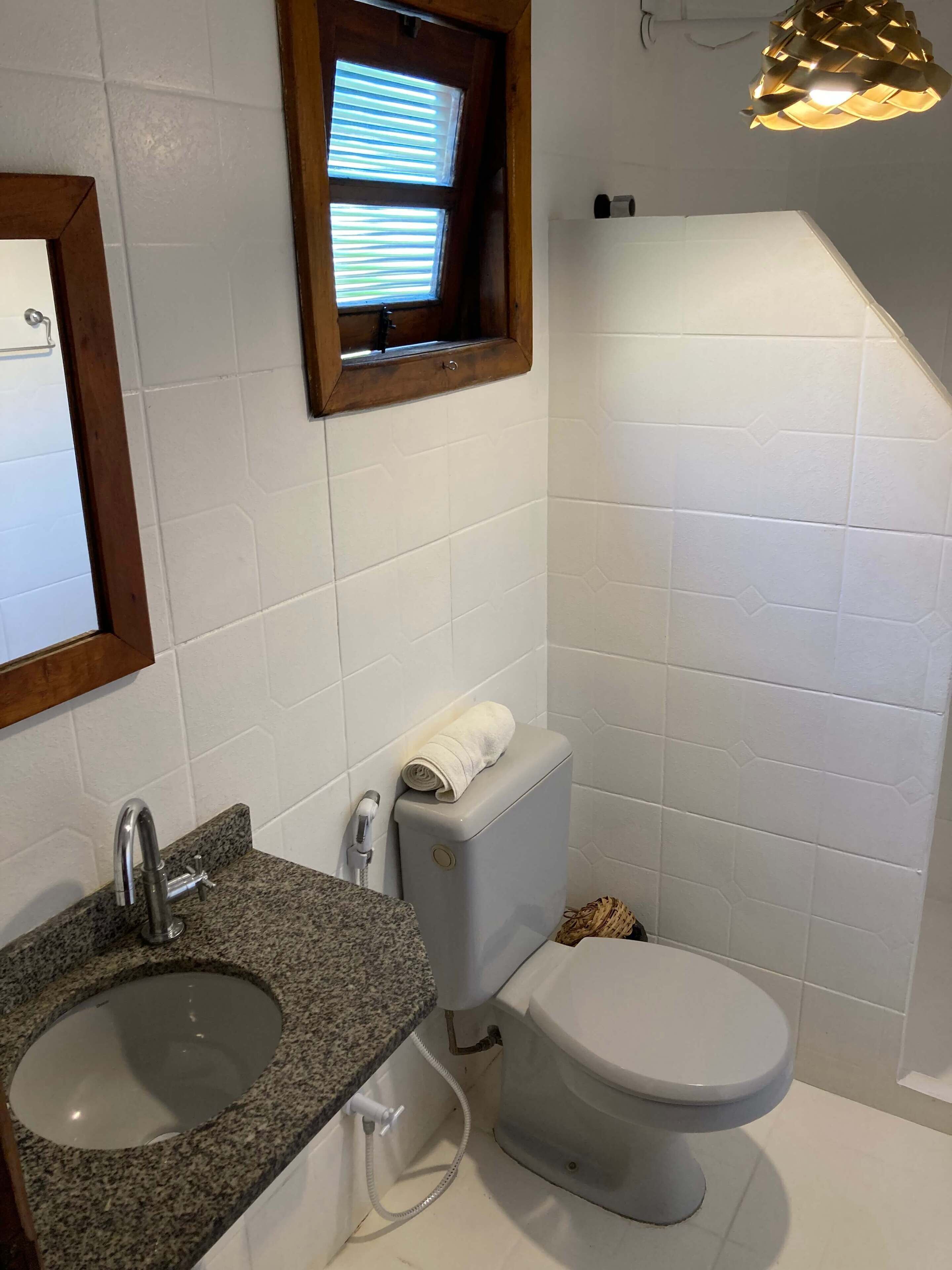 Un baño con lavamanos de granito, inodoro y ventana con persianas.
