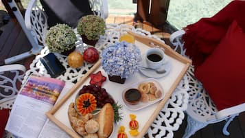 A table with a tray of food, including bread, grapes, and a small dish of jam, set on a white outdoor table with a book and decorative items.