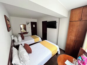 Ein Hotelzimmer mit zwei Betten, einem Schrank, einem Fernseher und einem kleinen Tisch.