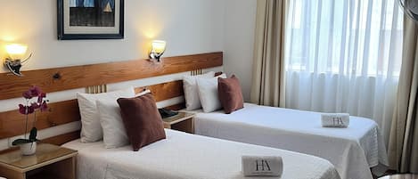 Habitación de hotel con dos camas, cabecero de madera, un cuadro en la pared y una ventana con cortinas.