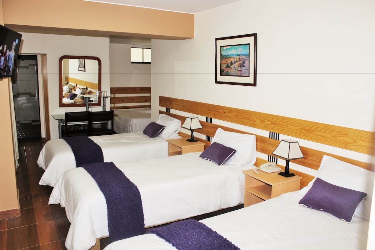 Ein Hotelzimmer mit drei Betten, einem Fernseher, einem Schreibtisch und einem Spiegel.