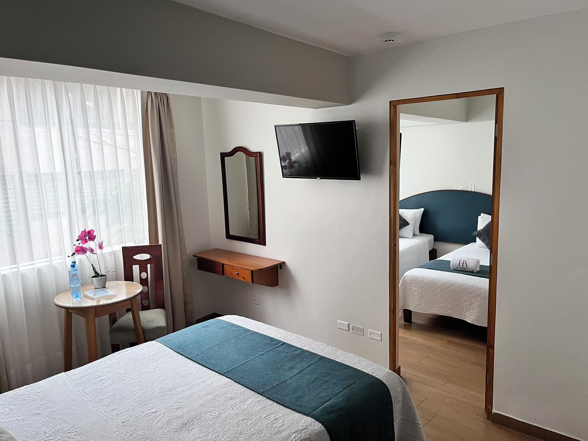 Una habitación de hotel con una cama, un escritorio, una silla, un espejo y un televisor.