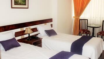 A hotel room with two beds, a nightstand, a lamp, a table with chairs, and a painting on the wall.