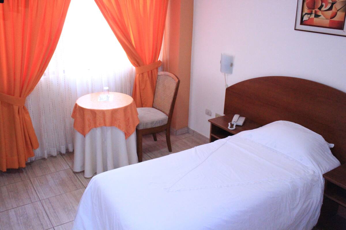 Ein Hotelzimmer mit einem Bett, einem Sessel, einem kleinen Tisch und einem Telefon auf dem Nachttisch.