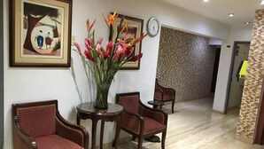 A hotel lobby with a reception desk, two chairs, a vase of flowers, and a clock on the wall. - Hotel Anthony's (Lima)