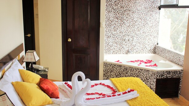 A hotel room with a bed, a nightstand, a lamp, a door, and a bathroom with a bathtub and a shower. - Hotel Anthony's (Lima)