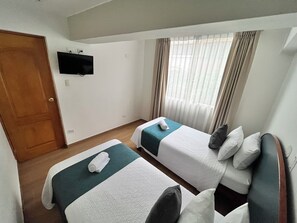 Ein Hotelzimmer mit zwei Betten, einem an der Wand befestigten Fernseher und einem Fenster mit Vorhängen.