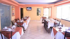 A restaurant with multiple tables and chairs, a television screen, and a tiled floor. - Hotel Anthony's (Lima)
