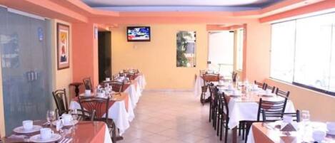 A restaurant with multiple tables and chairs, a television screen, and a tiled floor.