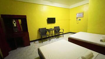 Une chambre d’hôtel avec des murs jaunes, un lit, un bureau avec deux chaises, une télévision et un petit meuble.